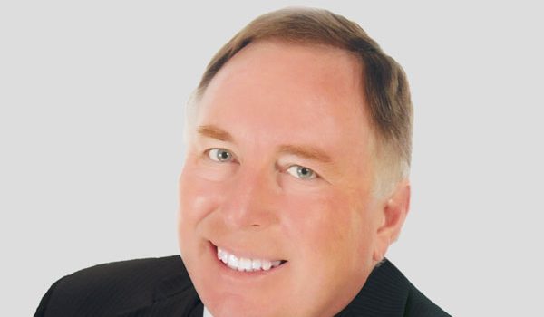 Smiling businessman in a dark suit and striped tie against a light gray background.