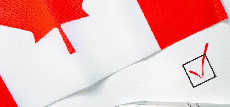 Close-up of a white surface with a red checkmark in a square box beside a silver pen, suggesting a ballot or form.