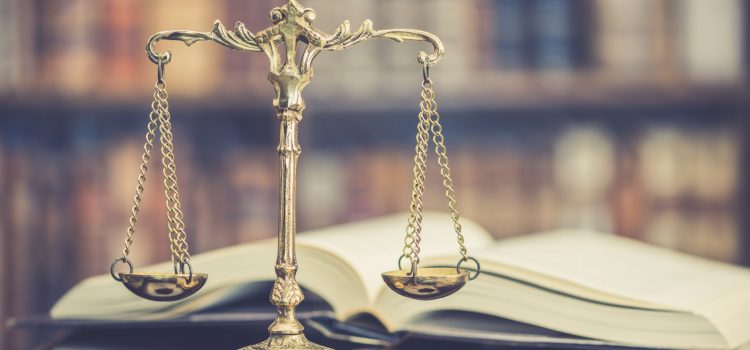 Bronze balance scales resting on an open law book with blurred books in the background