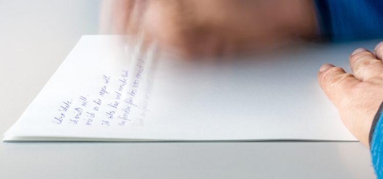 Blurred close-up of a hand writing on a white notebook with blue ink, motion suggests handwriting activity