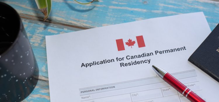 Form for Canadian Permanent Residency on a blue wooden table, with a red pen and a plant nearby.
