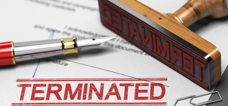 Close-up of a wooden stamp stamped with 'TERMINATED' on a document, with a red-tipped pen nearby, conveying termination of status or contract.
