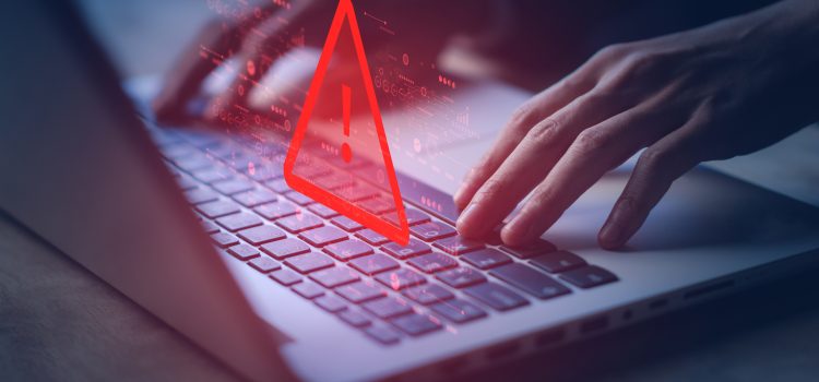Hands typing on a laptop keyboard with a glowing red warning triangle overlay signaling a cybersecurity alert