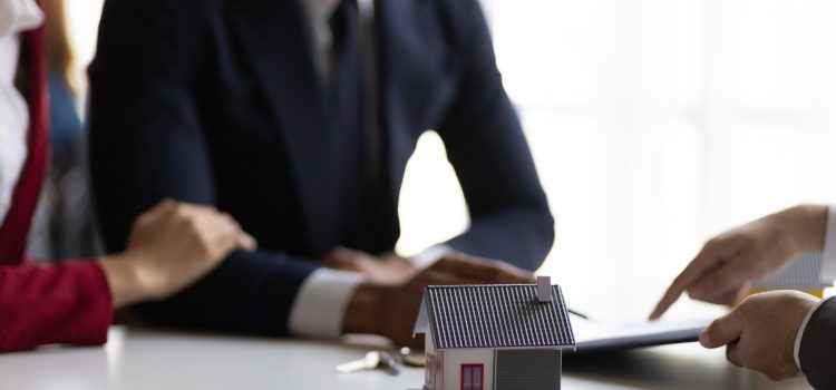 Group of professionals in business attire discussing a small house model on a table.