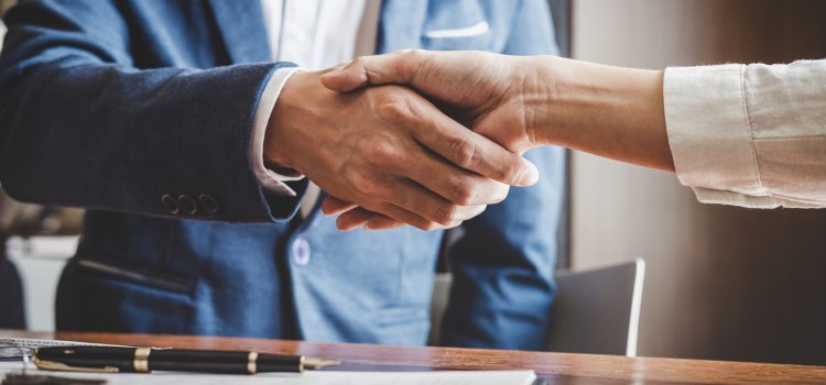 Two people shake hands over a desk with a pen and documents, signaling agreement in a business setting.