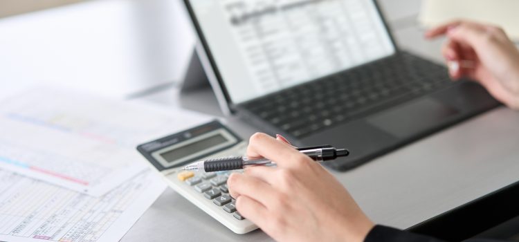 Person using a calculator on a desk with a laptop and financial documents nearby, focused on calculations.