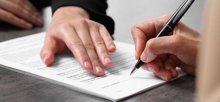 Close-up of hands signing a printed document with a black pen on a desk.