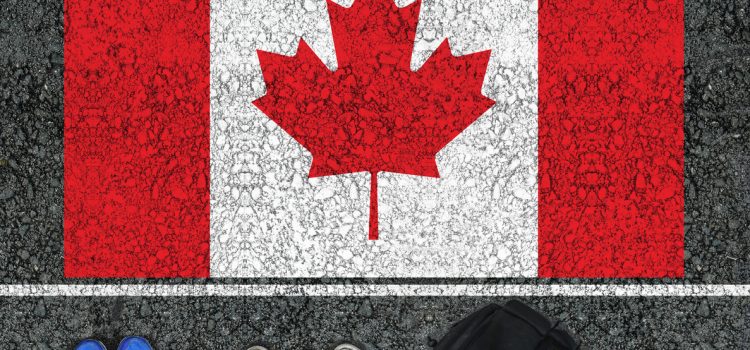 People's feet standing along the edge of a Canadian flag painted on asphalt.