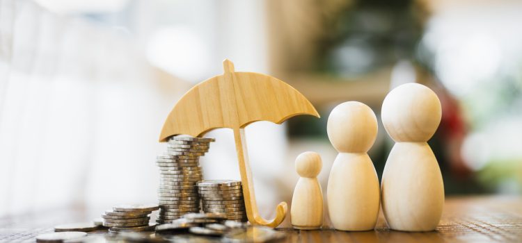 Wooden family figurines beside a stack of coins and a small wooden umbrella, symbolizing family finances and savings protection.