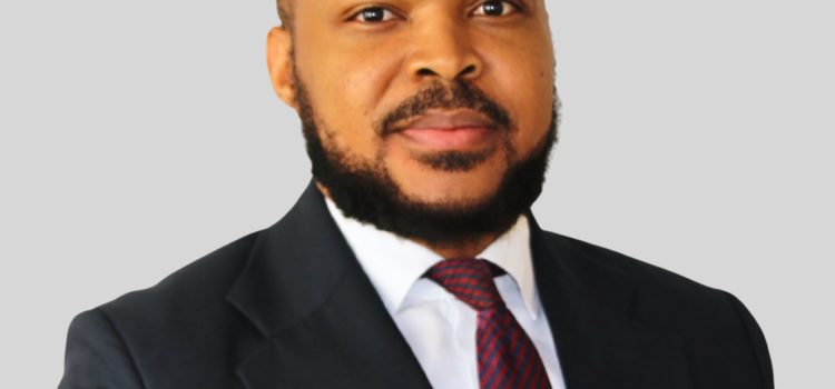 Professional headshot of a man in a dark suit and red striped tie against a gray background, facing the camera.