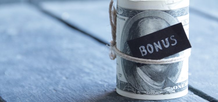 Close-up of a rolled one-dollar bill tied with twine and a black 'BONUS' tag, on a blue wooden surface.