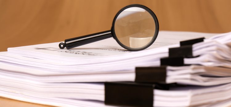 Magnifying glass resting on a stack of printed documents with black binder clips.
