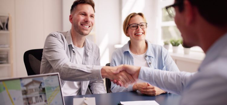People in a bright office shake hands across a table, smiling during a meeting.