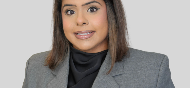Professional portrait of a woman in a gray blazer and black blouse, neutral background, ready for a corporate profile.