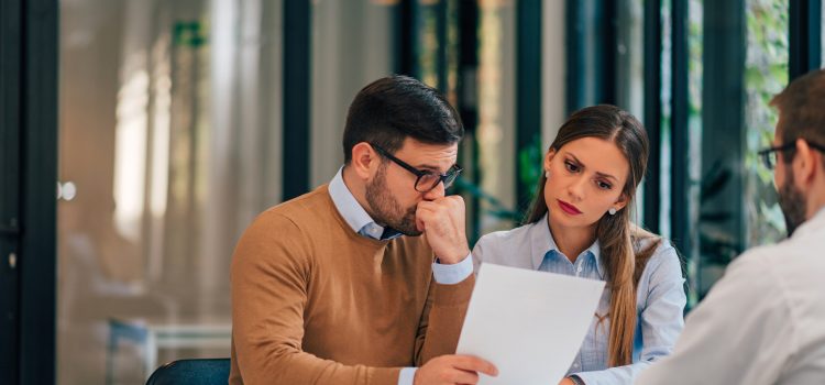 Worried couple looking at paper document in the office of financial adviser.